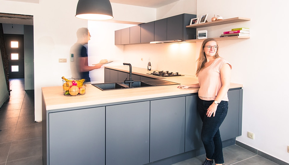 Une cuisine moderne avec des armoires grises, un plan de travail en bois clair, un évier noir, et des étagères murales avec des livres.