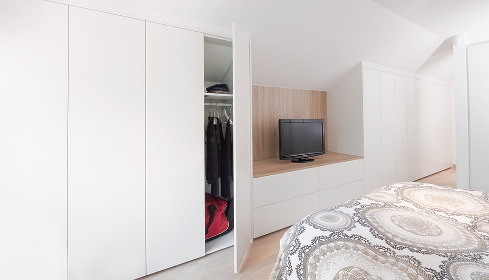 Placard blanc ouvert avec vêtements suspendus, télévision sur meuble en bois clair, lit avec couverture à motifs circulaires.