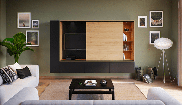 Meuble mural noir et bois avec télévision et étagères, entouré de cadres photo, dans un salon moderne avec canapé blanc et plante verte.