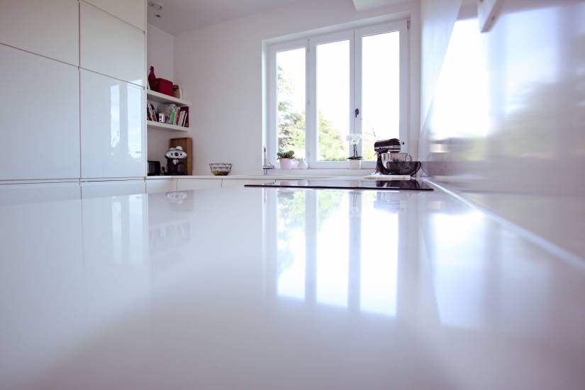 Cuisine moderne avec plan de travail blanc brillant, fenêtre à double battant et étagères contenant livres et machine à café.