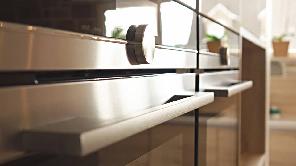 Poignées métalliques d'un four moderne encastré dans une cuisine, avec des plantes en arrière-plan.