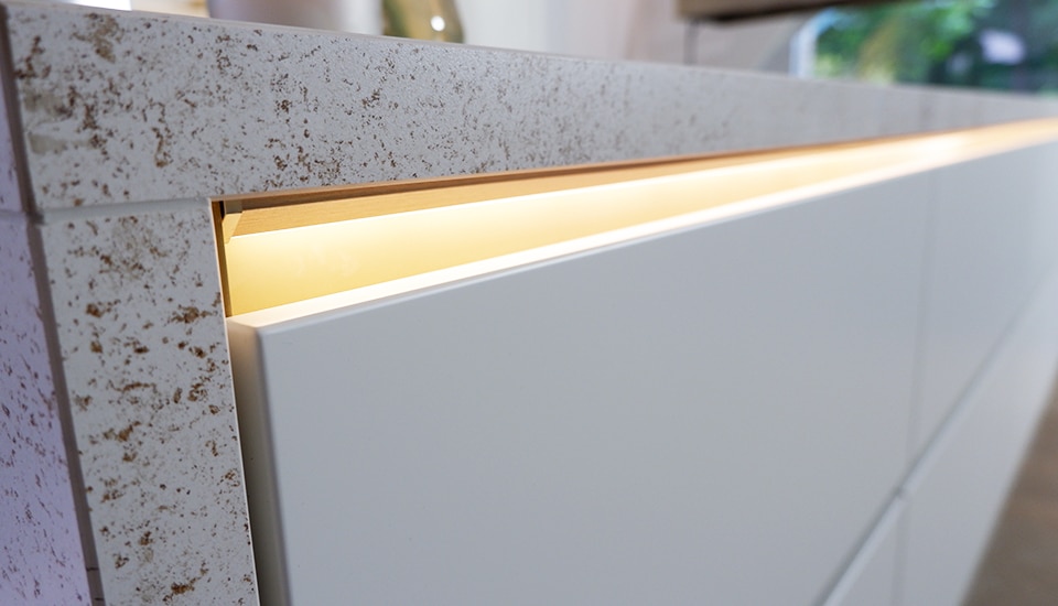 Un plan de travail en pierre beige avec des tiroirs blancs éclairés par une lumière LED intégrée, vue en gros plan.