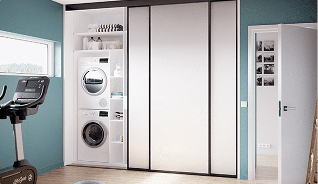 Machine à laver et sèche-linge blancs encastrés dans une armoire blanche, à côté d'un vélo d'appartement noir dans une pièce aux murs verts.