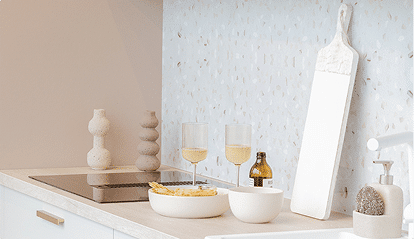 Plan de travail de cuisine avec planche à découper blanche, verre de vin, bol de chips et bouteille en verre ambré.