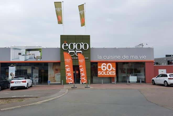 Façade d'un magasin èggo avec des bannières orange affichant "60% soldes", entourée de voitures blanches et grises sur un parking.