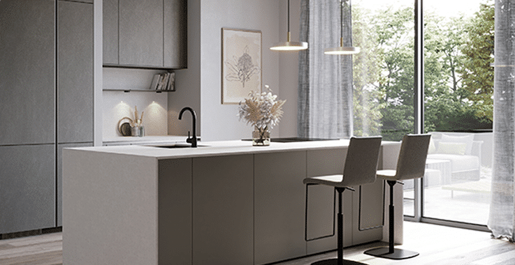 Cuisine moderne avec îlot central gris, deux tabourets, luminaires suspendus et grandes fenêtres donnant sur un jardin verdoyant.