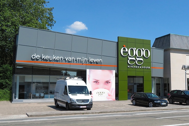 Magasin èggo avec façade grise et verte, camionnette blanche et voiture noire stationnées devant.