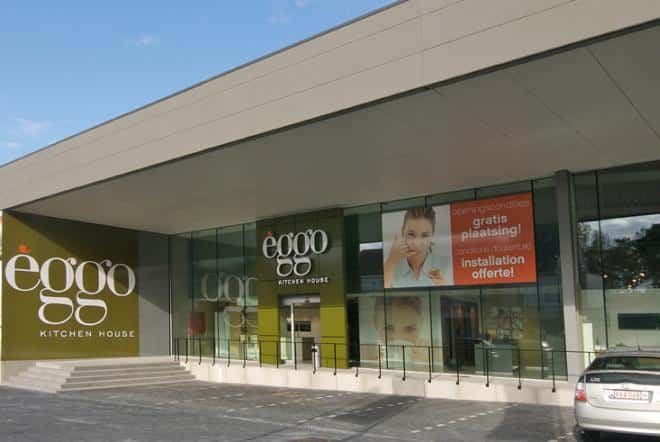 Façade d'un magasin éggo avec des panneaux de verre, un logo blanc et orange, et une voiture stationnée devant.