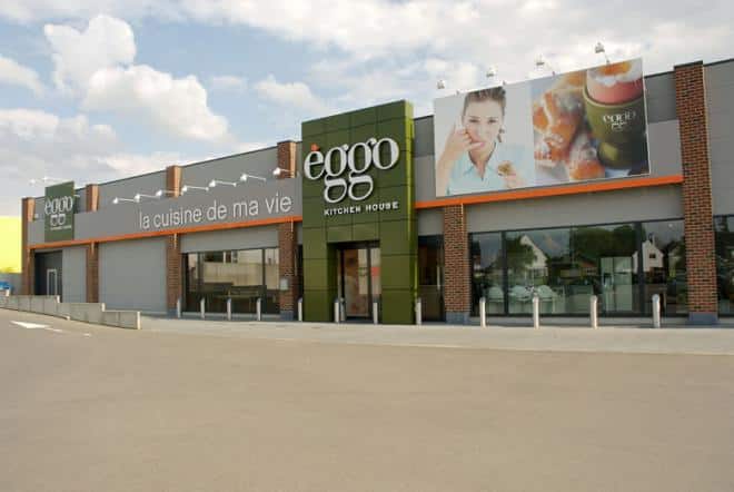 Façade d'un magasin èggo avec enseignes et vitrines, murs en briques rouges et panneaux publicitaires sur fond de ciel nuageux.
