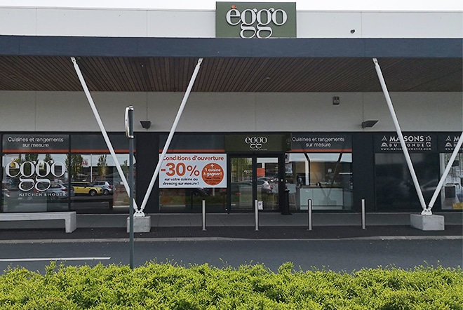 Façade d'un magasin èggo avec vitrine affichant une promotion de -30% sur les cuisines, entourée de structures blanches et d'arbustes verts.