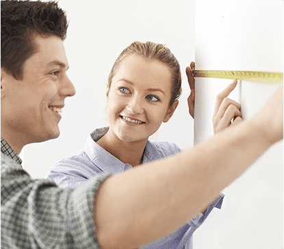 Deux personnes mesurent un mur blanc avec un ruban à mesurer jaune. L'une d'elles tient l'extrémité du ruban.