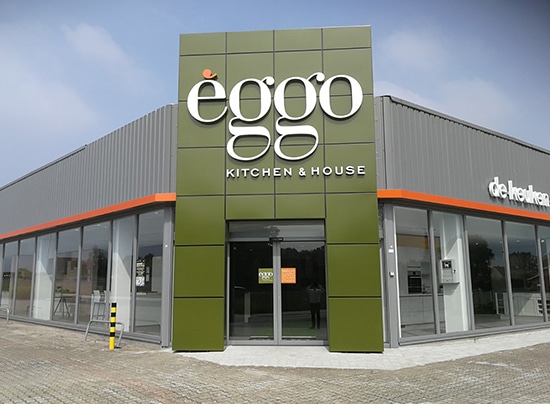 Façade d'un magasin èggo avec un panneau vert et blanc, entouré de vitrines et d'un bâtiment gris avec une ligne orange.