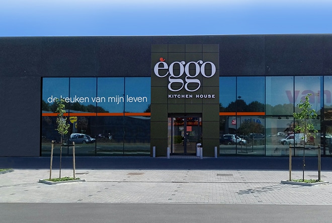 Façade d'un magasin éggo avec grandes vitrines, logo blanc sur fond noir, et quelques jeunes arbres plantés devant.