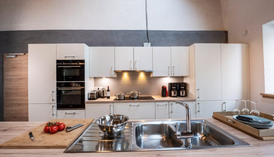 Cuisine moderne avec des placards blancs, un plan de travail en bois clair, des appareils électroménagers en acier inoxydable et des tomates sur une planche à découper.