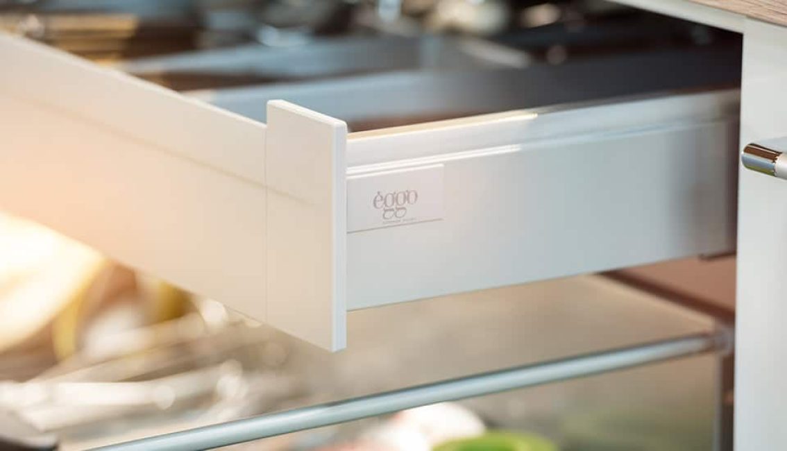 Tiroir de cuisine blanc ouvert avec poignée métallique, contenant des ustensiles visibles à l'intérieur, éclairé par une lumière douce.