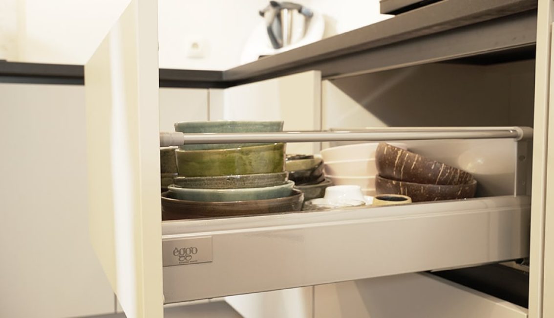 Tiroir de cuisine ouvert avec des assiettes vertes et brunes empilées à côté d'un appareil électroménager blanc.