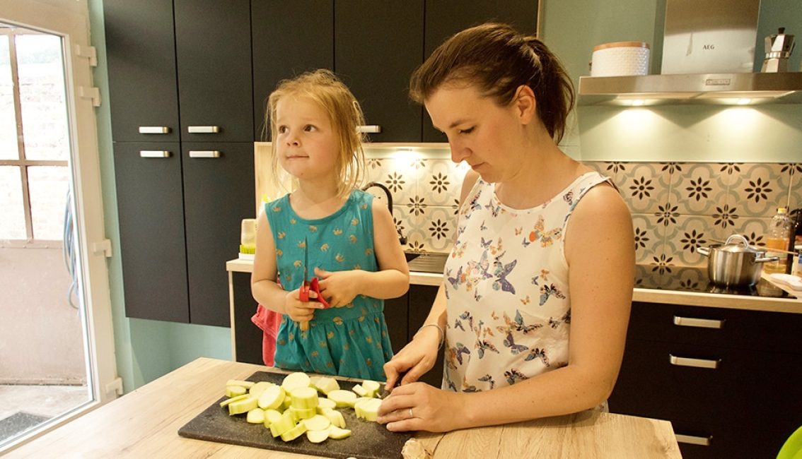 Une femme et une enfant préparent des pommes sur une planche dans une cuisine moderne avec des armoires noires et un dosseret floral.