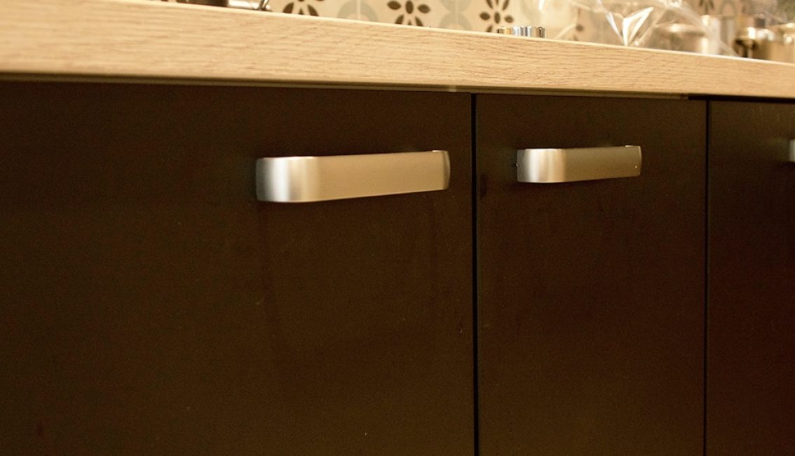 Portes de placard noires avec poignées métalliques sous un plan de travail en bois clair, carrelage à motifs en arrière-plan.